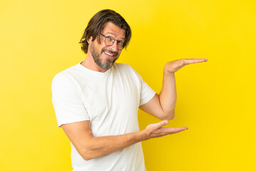 Senior dutch man isolated on yellow background holding copyspace to insert an ad