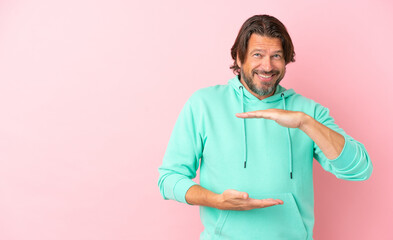 Senior dutch man isolated on pink background holding copyspace imaginary on the palm to insert an ad