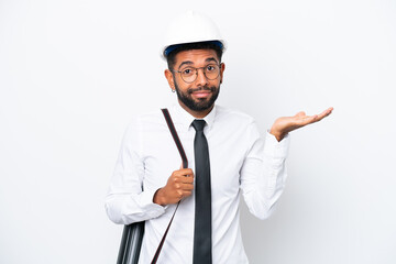 Young architect Brazilian man with helmet and holding blueprints isolated on white background having doubts while raising hands