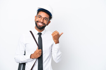 Young architect Brazilian man with helmet and holding blueprints isolated on white background pointing to the side to present a product