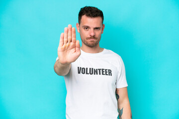 Young volunteer caucasian man isolated on blue background making stop gesture