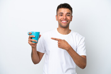 Young Brazilian man holding cup of coffee isolated on white background and pointing it