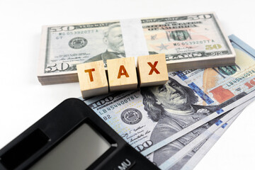 Tax text on wood block with calculator and paper money bill