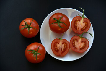 Ripe beautiful tomato fruit on a white plate top view. Delicious tomatoes still life.