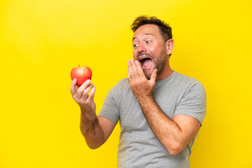 Middle age caucasian man with an apple isolated on yellow background with surprise and shocked...