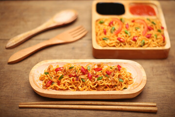 Instant fried noodles with soy sauce and spicy chili sauce in bowl on wooden table background. Top view.