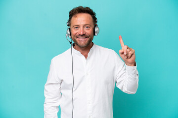 Telemarketer caucasian man working with a headset isolated on blue background showing and lifting a finger in sign of the best