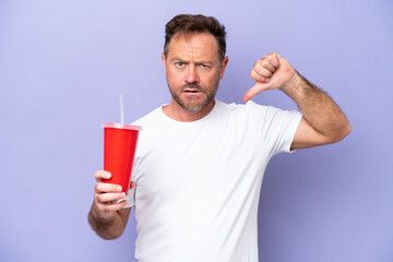 Middle age caucasian man holding soda isolated on purple background showing thumb down with...