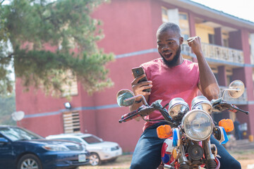 african bike man rejoices while checking his phone