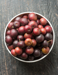 bowl full of governor's plum fruits, flacourtia indica, also known as ramontchi, madagascar plum or indian plum,reddish black fleshy fruits taken from above with copy space