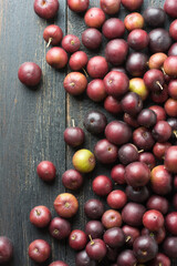 scattered governor's plum fruits on a black rustic table top, flacourtia indica, also known as ramontchi, madagascar plum or indian plum, reddish black fleshy fruits taken from above with copy space