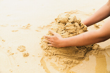 On a sandy beach, a man's hands are gathering sand to make a pile of sand. Playing sand piles is...