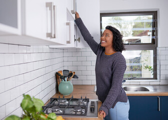 A young multi-ethnic woman reaches into her kitchen cupboards - Powered by Adobe