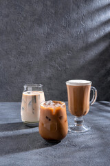 Ice coffee in a tall glass with cream poured over and coffee beans. Cold coffee drink on a dark background with copy space. Set with different types of coffee drinks on a dark table.