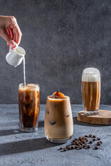Milk Being Poured Into Iced Coffee on a dark table. Ice coffee in a tall glass with cream poured...