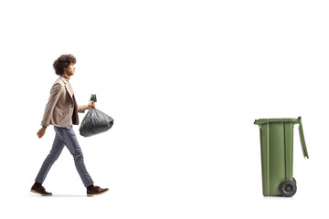 Full length profile shot of a tall young man walking towards a bin and carrying a plastic bag