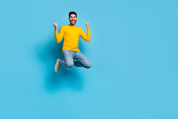 Full length portrait of delighted excited man jump raise fists celebrate success isolated on blue...