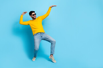 Full length photo of cool funny guy dressed yellow pullover dark eyewear having fun empty space isolated blue color background