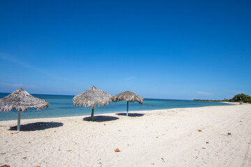Paradise beach in Cuba with palm umbrella and clear blue water. 