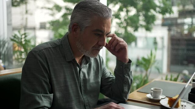 Annoyed businessman in front of computer working at coffee shop. Senior executive typing message response