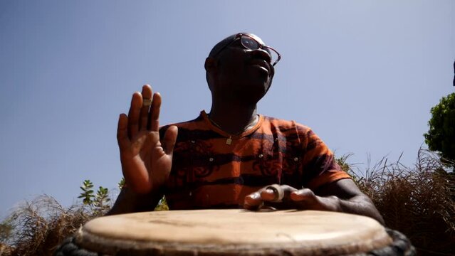 Slow motion footage of man playing djembe from the front at ankle height looking up