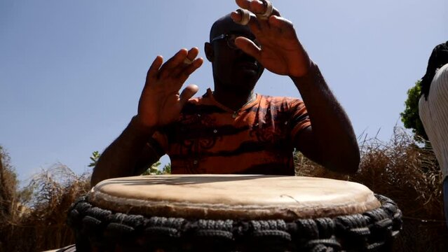 Slow motion footage of man playing djembe from the front at ankle height looking up