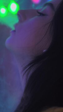 Color light. The girl smokes a vape releases a lot of steam. Vertical video