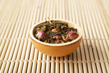 Stringed tea bowl with roses in the foreground on bamboo mats 