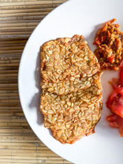 fried tempeh with slices tomato and chilli sauce on a white plate.