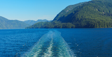 Ship's wake on ocean with BC coastline and mountain backdrop.