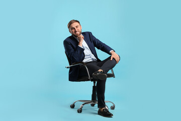 Young businessman sitting in comfortable office chair on turquoise background - Powered by Adobe