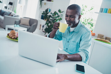 Portrait of positive peaceful man enjoy fresh hot coffee use wireless netbook coworking kitchen indoors