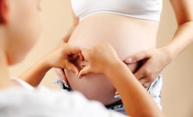 Little boy making a heart shape on the pregnant belly with his hands : Concept of pregnancy