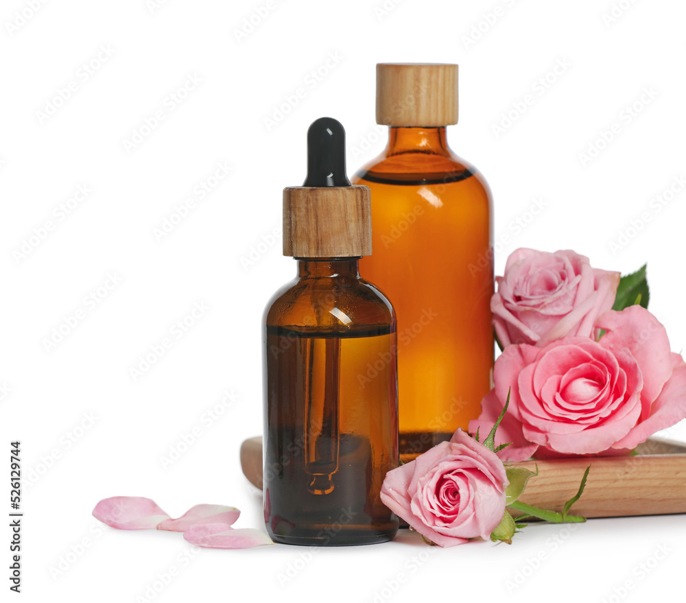 Wall mural bottles of essential rose oil and flowers on white background