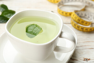 Cup of diet herbal tea with green leaf on white wooden table, closeup