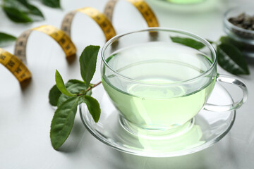 Cup of herbal diet tea and measuring tape on light table