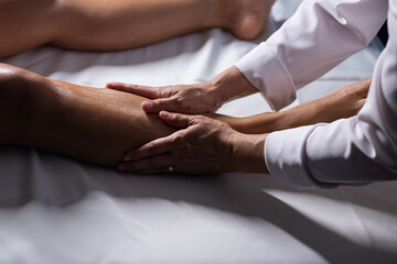 Um profissional fazendo massagem terapeutica nas pernas do paciente que está deitado em uma maca. - obrazy, fototapety, plakaty