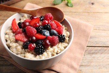 Bowl with tasty oatmeal porridge and berries served on wooden table, closeup. Healthy meal