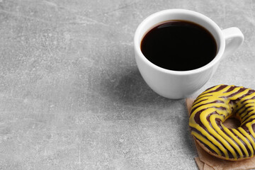 Tasty frosted donut and cup of coffee on light grey table, space for text