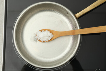 Frying pan with coconut oil and wooden spatula on induction stove, top view. Healthy cooking