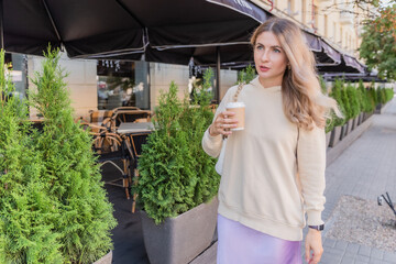 Fototapeta premium The girl is going on the street with craft cup of coffee