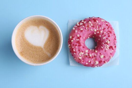 Tasty frosted donut and cup of coffee on light blue background, flat lay