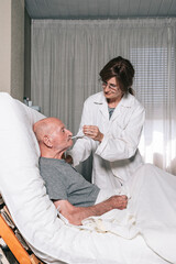 Nurse giving medication to an elderly person lying on a bed