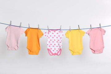 Colorful baby onesies drying on laundry line against light background