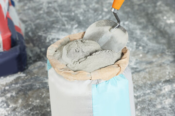 Cement powder and trowel put in bag on stone floor, closeup