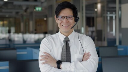 Portrait of smart asian male customer service representative with headset, smile face and stand at call center room. Looking to camera.