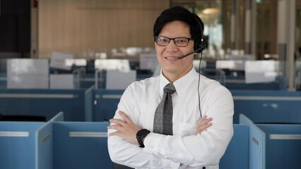 Portrait of smart asian male customer service representative with headset, smile face and stand at call center room. Looking to camera.