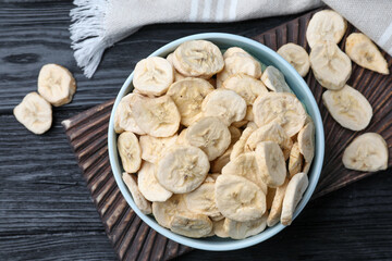 Bowl and dried banana slices on black wooden table, top view