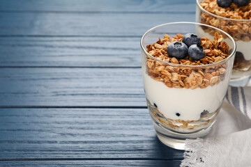 Glasses of tasty yogurt with muesli and blueberries on blue wooden table. Space for text