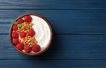 Bowl of tasty yogurt with raspberries and muesli served on blue wooden table, top view. Space for...